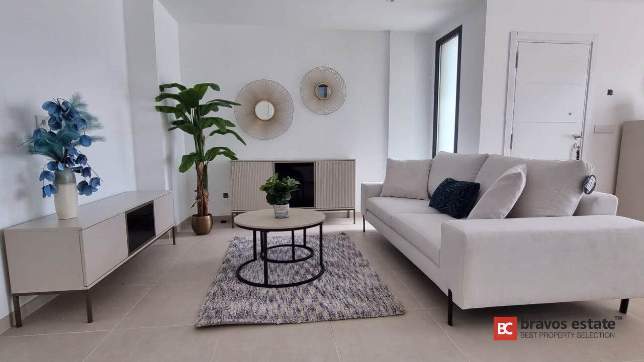 Musterwohnzimmer in Aura Finestrat mit hellem Sofa, Sideboard, Pflanzendeko und Fliesenboden