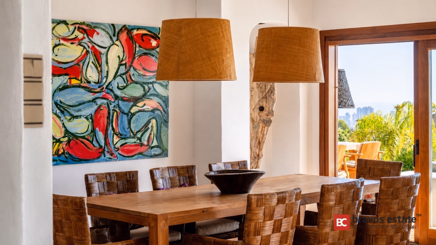 Massivholz-Esstisch mit geflochtenen Stühlen und großem abstrakten Gemälde in Villa Ibiza