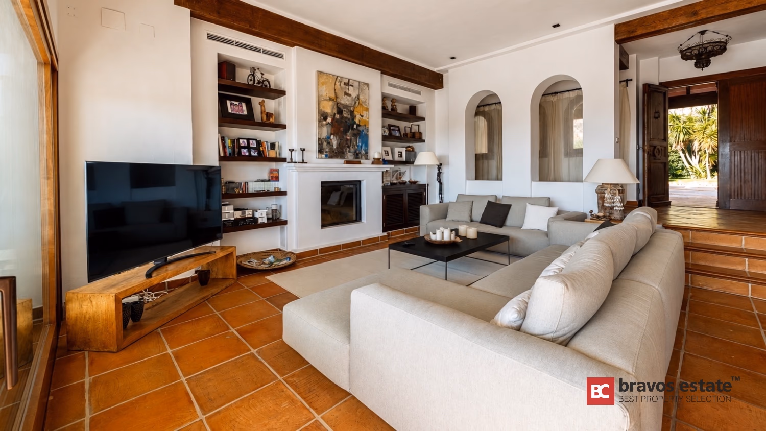 Wohnzimmer der Villa Ibiza mit TV, Kamin, Einbauregalen und rustikalem Terrakottaboden