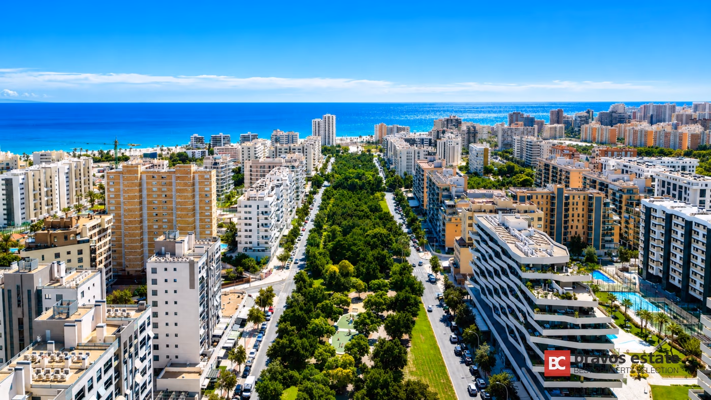 Aerial view of PAU 5 in Playa de San Juan, Alicante — modern apartment blocks lined along the central park strip and Avenida Maestro Garberí, with the Mediterranean Sea in the background