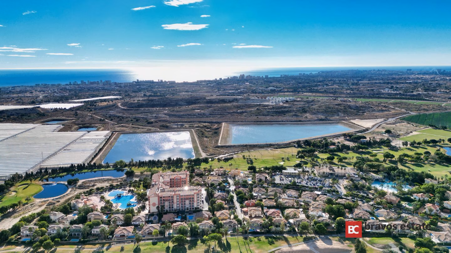 Vista aérea del entorno del resort de golf Bonalba Green en Mutxamel, con el hotel del resort, villas, calles de golf, lagunas y el mar Mediterráneo al fondo.