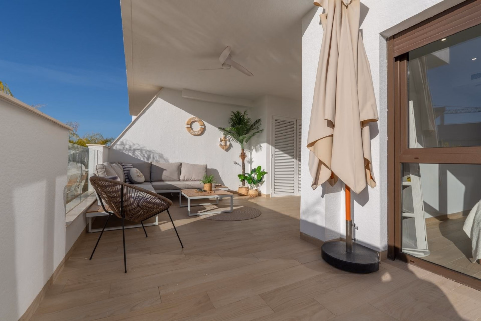 Terrace with wicker armchairs, parasol and the sliding doors of the apartment
