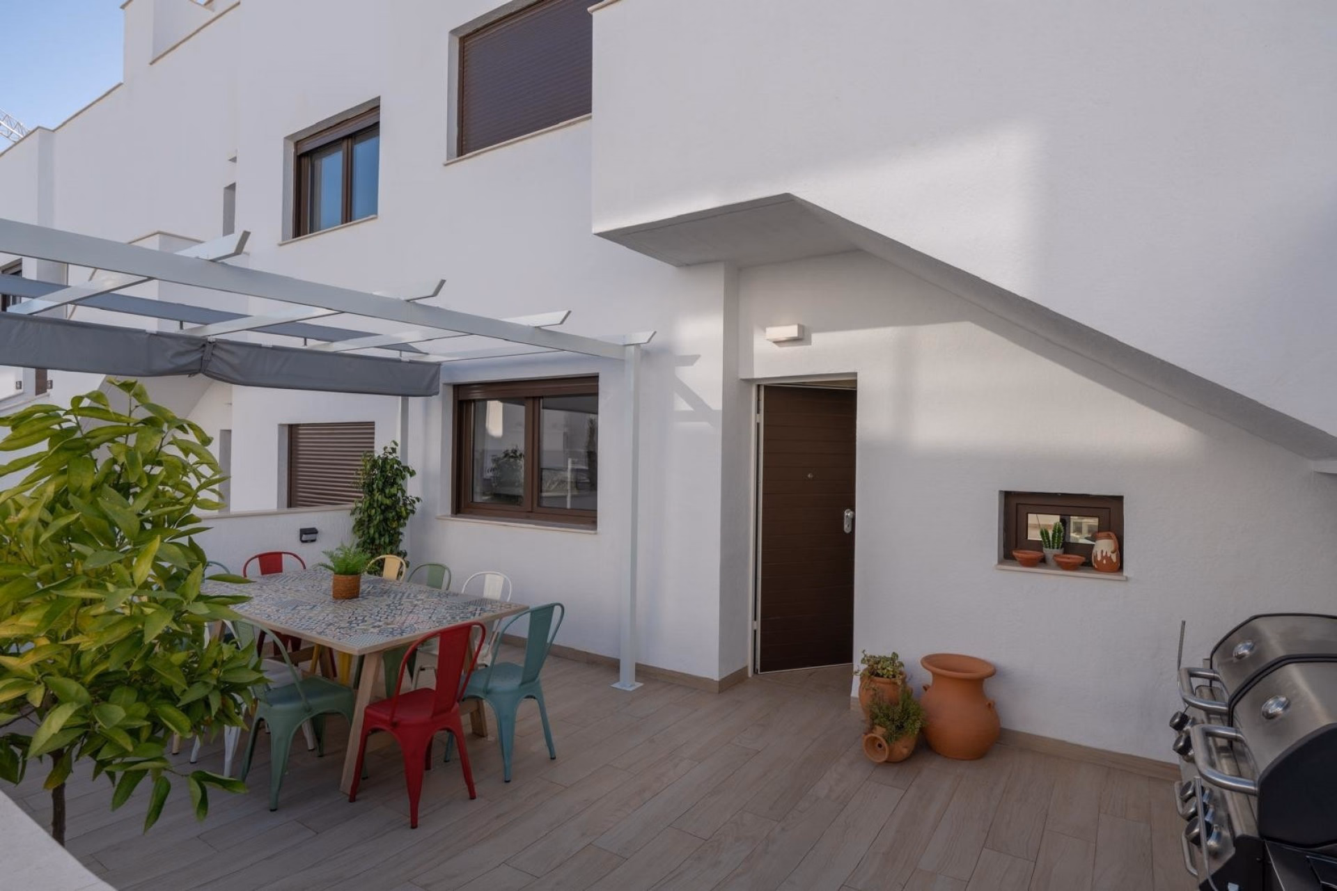 Side terrace with a dining table under a pergola and a barbecue