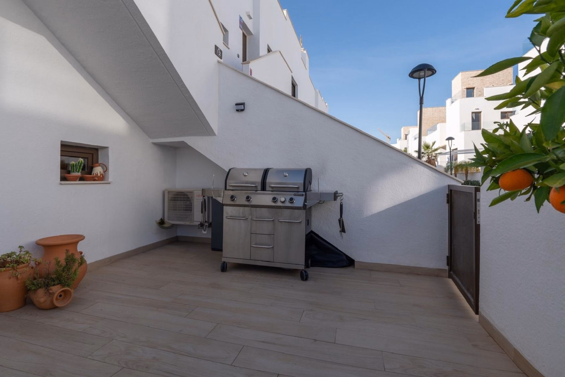 Paved terrace with a gas barbecue, potted plants and a white wall