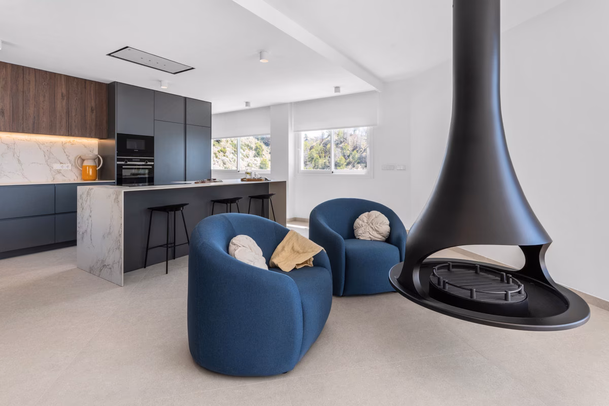 Chimenea suspendida y sillones azules junto a la cocina
