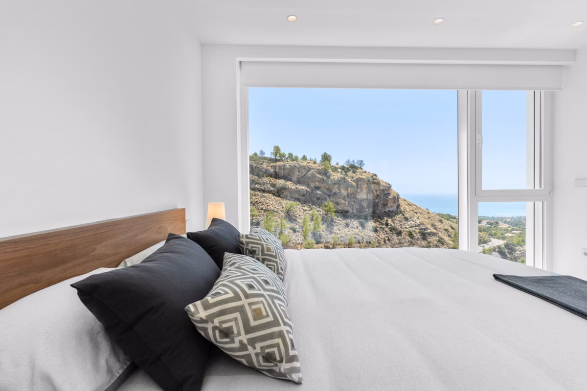 Dormitorio con ventanal a las colinas arboladas y el mar