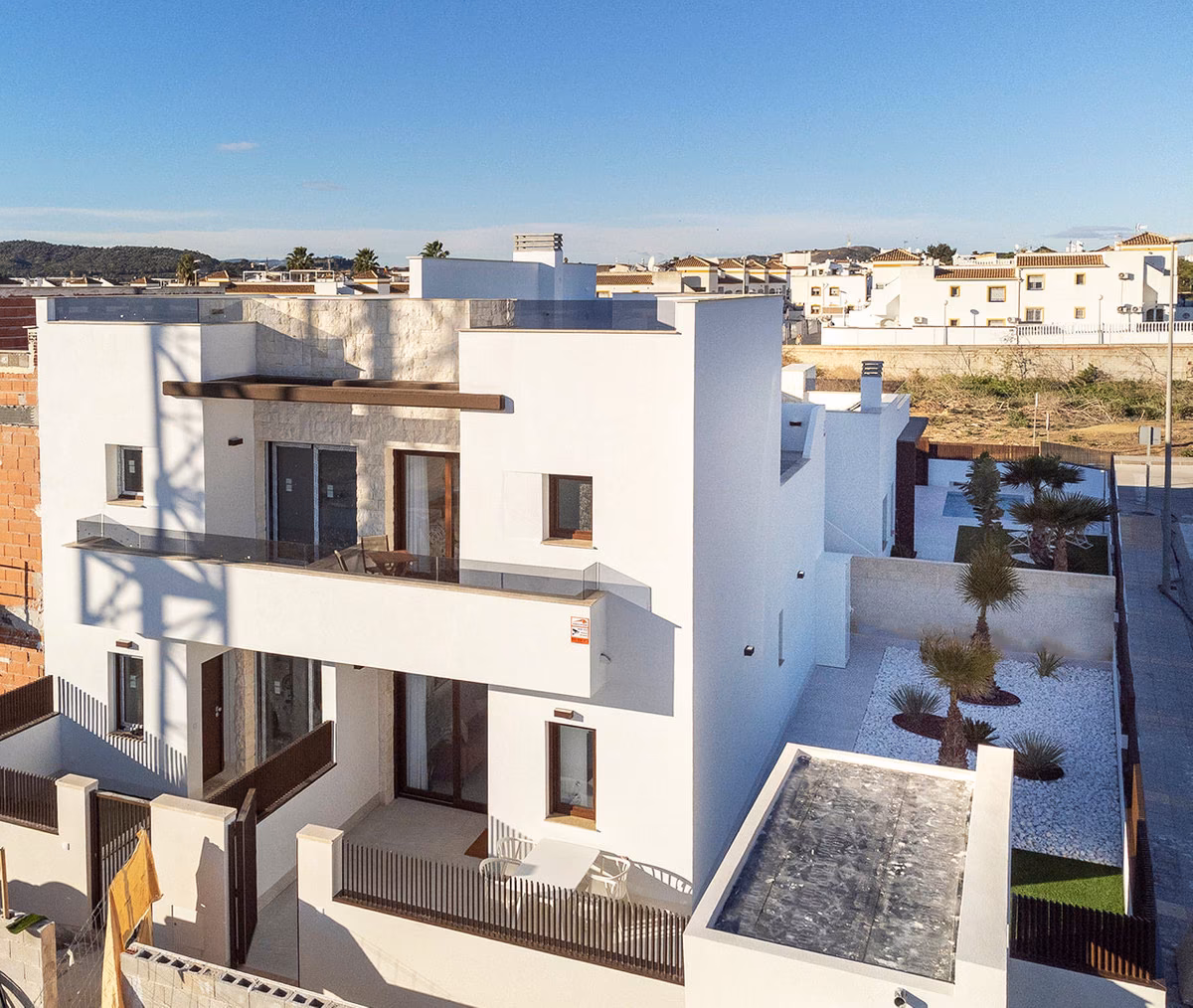 Aerial view of the two-storey white villa with a first-floor terrace and a landscaped side garden