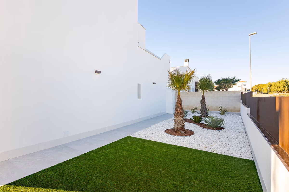 Side garden with artificial lawn, white gravel and palm trees