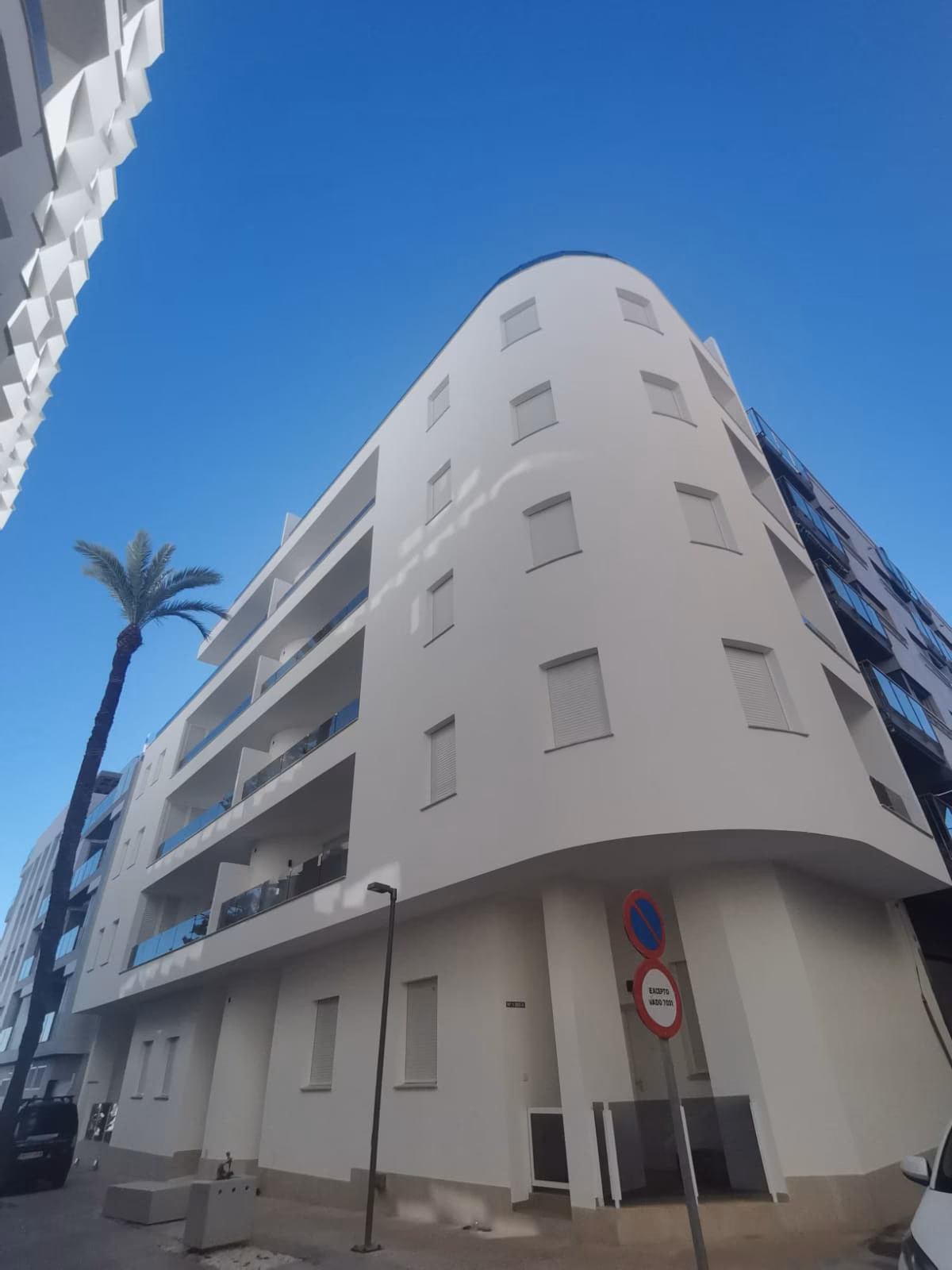 Ecke des weißen Wohnhauses mit geschwungenen Balkonen, von der Straße aus