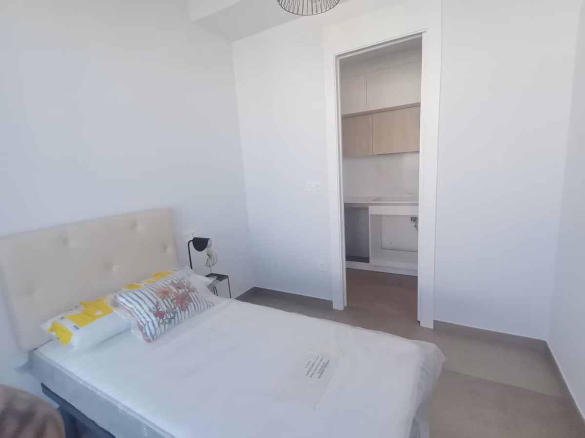 Schlafzimmer mit gepolstertem Kopfteil, durch die Tür die Küche