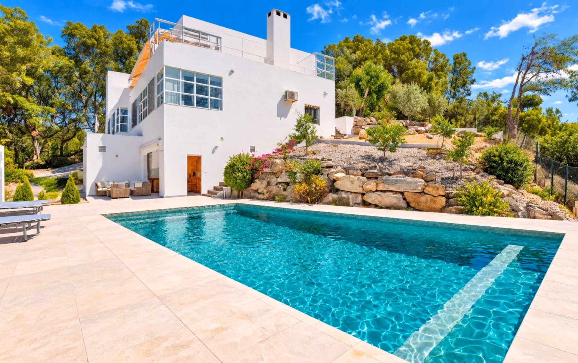 Villa facade with large windows rising above the pool terrace and rock garden