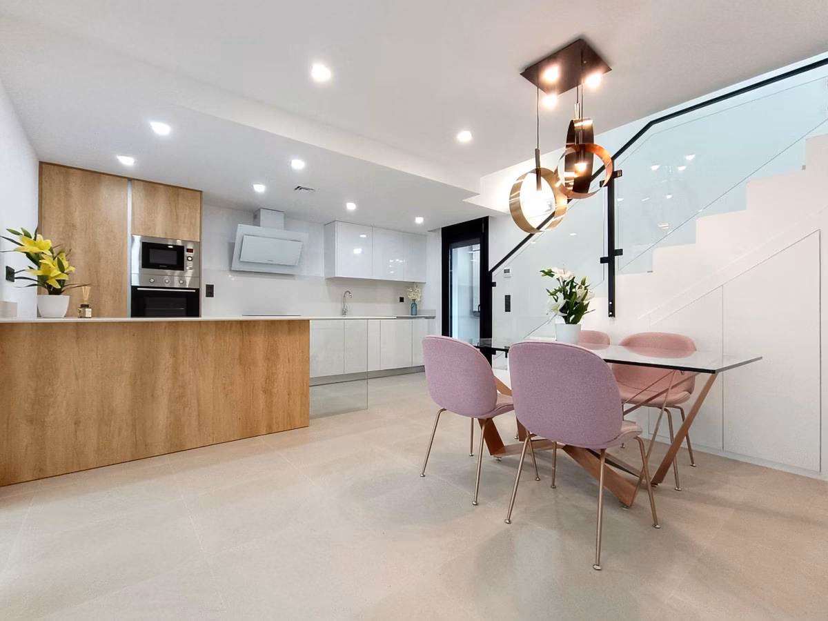 Cocina blanca de alto brillo con isla efecto madera y escalera con barandilla de vidrio