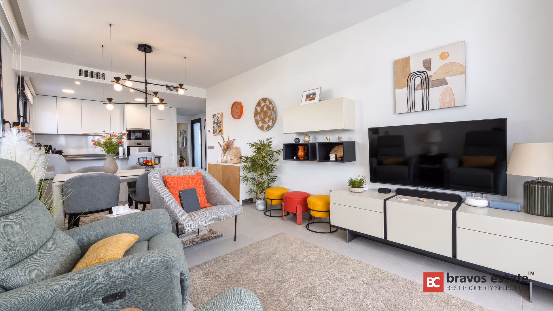 Salon avec meuble TV, fauteuils et la cuisine visible dans l'espace ouvert
