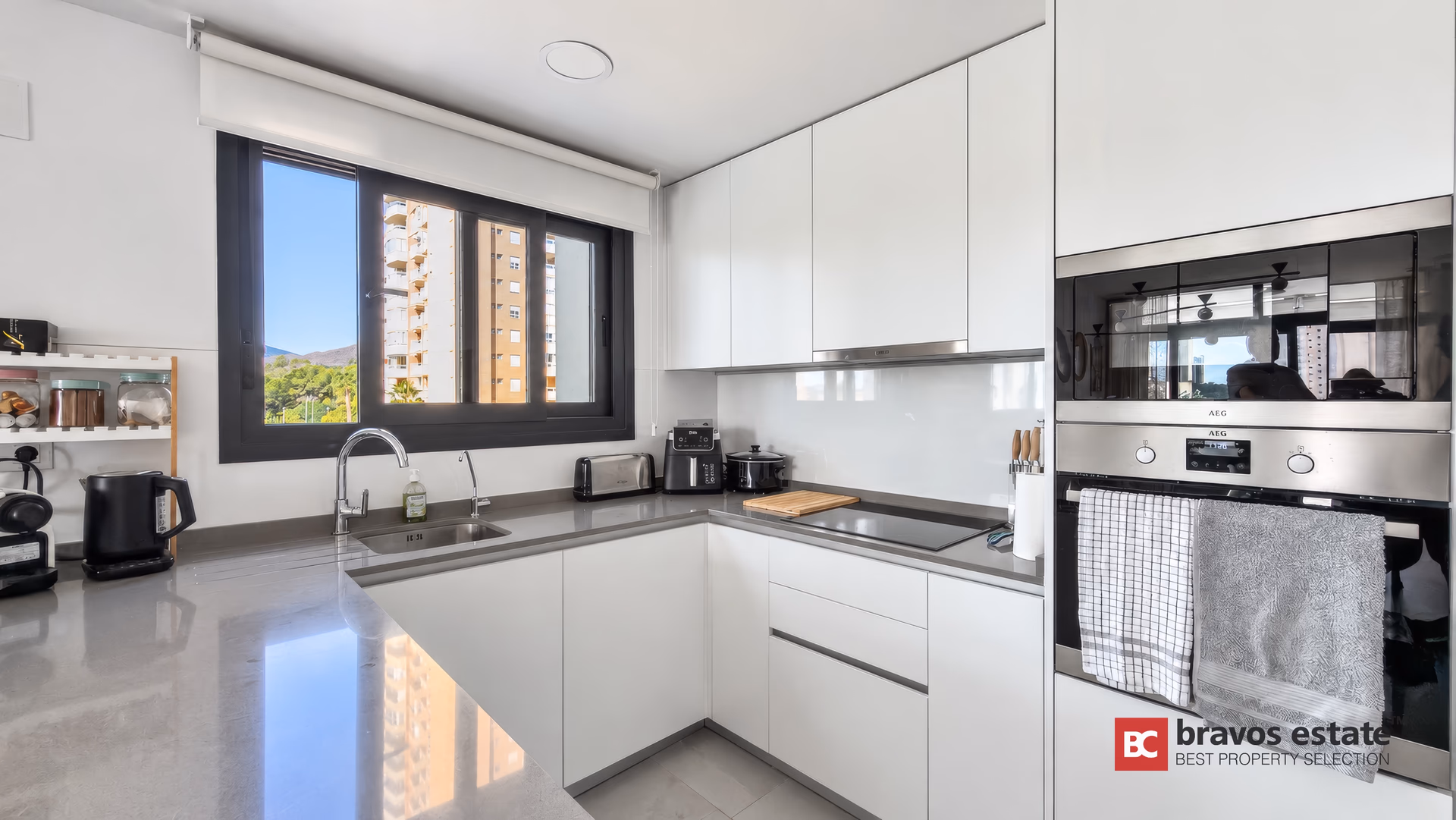 Cuisine blanche avec four encastré, plaque à induction et fenêtre avec vue sur la ville