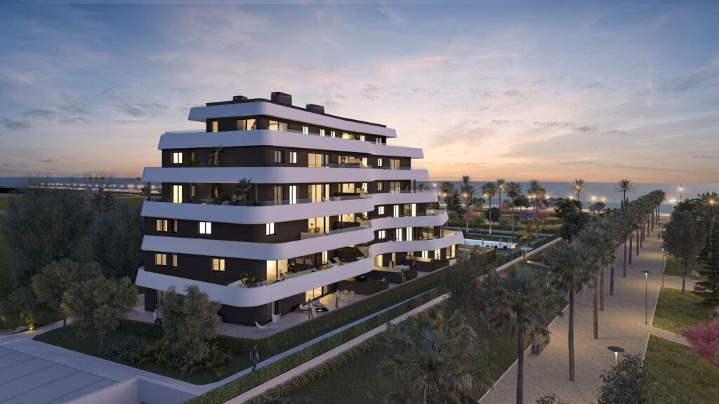 Wohnblock mit gestaffelten Terrassen zwischen Gärten bei Sonnenuntergang, in der Ferne das Meer