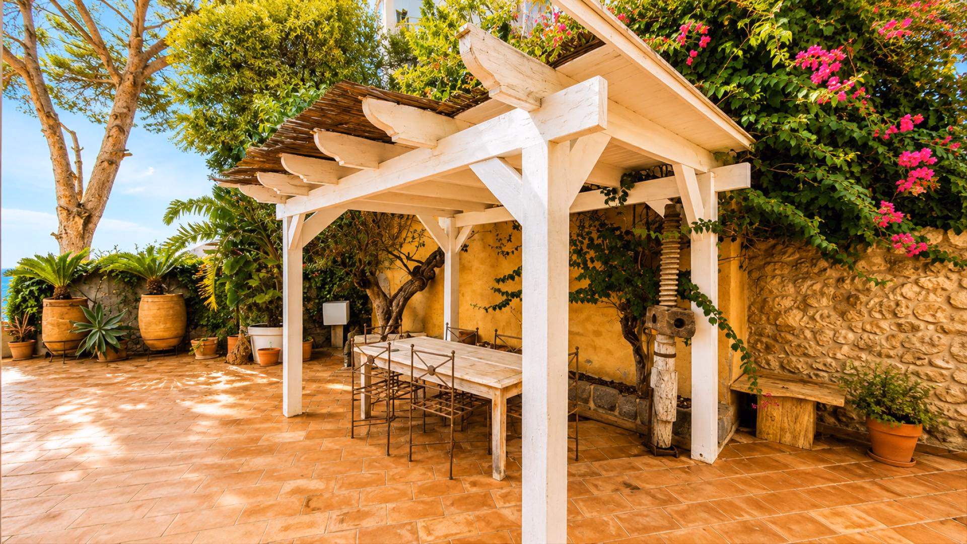 Gartenterrasse mit Holzpergola, Esstisch und blühenden Pflanzen