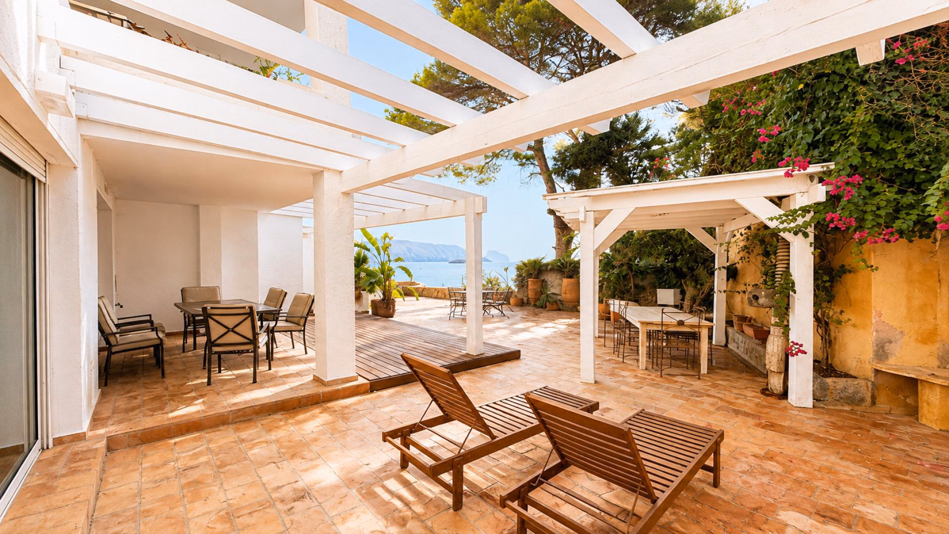 Terrasse mit Sonnenliegen unter einer weißen Pergola und Meerblick