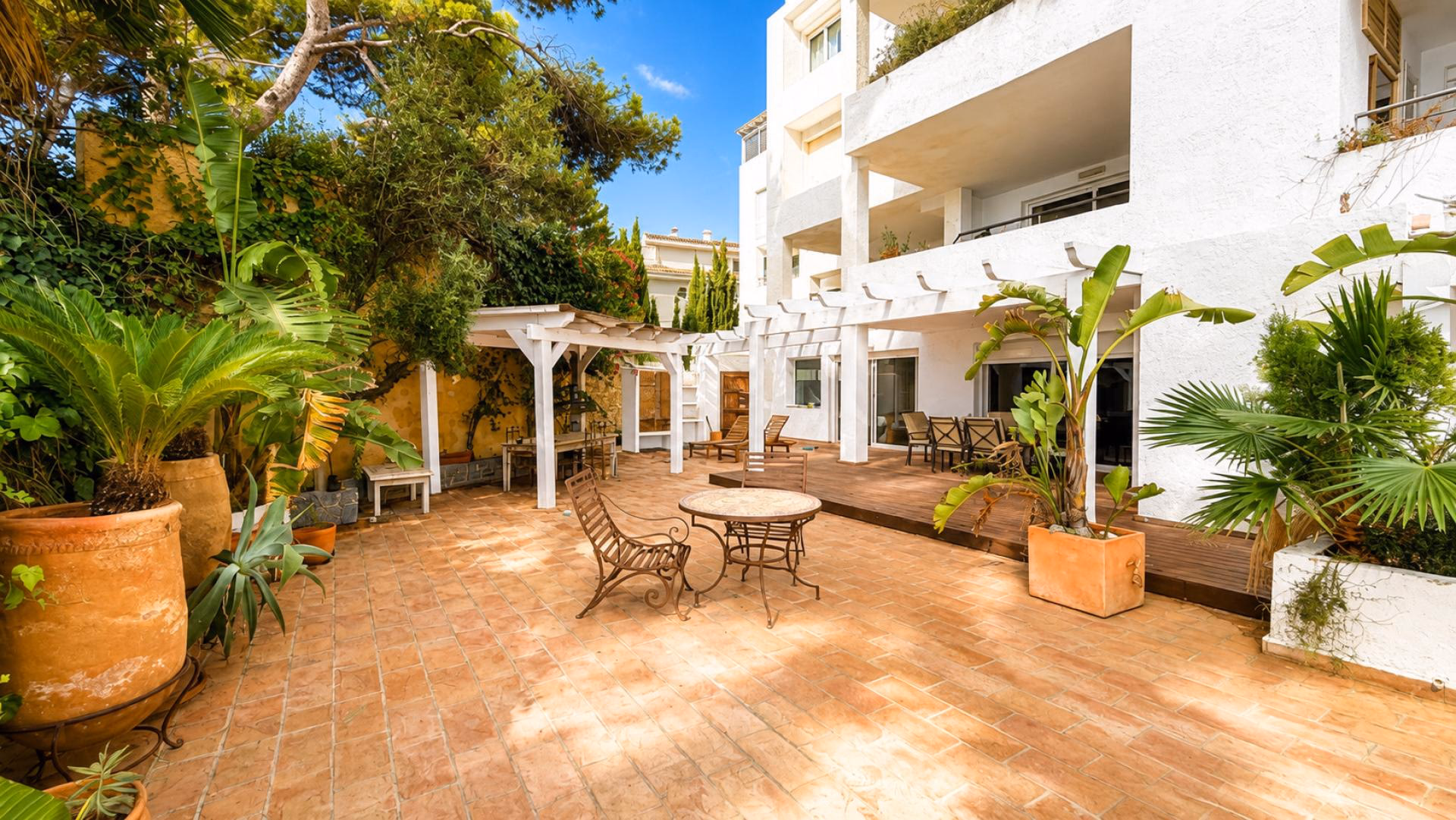 Patio mit rundem Tisch, Pflanzkübeln und der weißen Fassade des Hauses