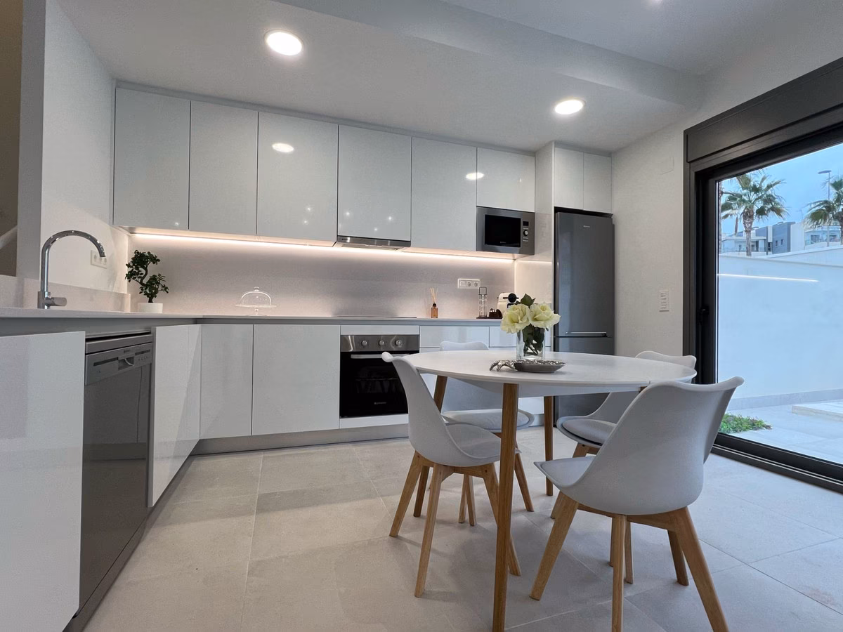 Fitted white kitchen with round dining table and garden view