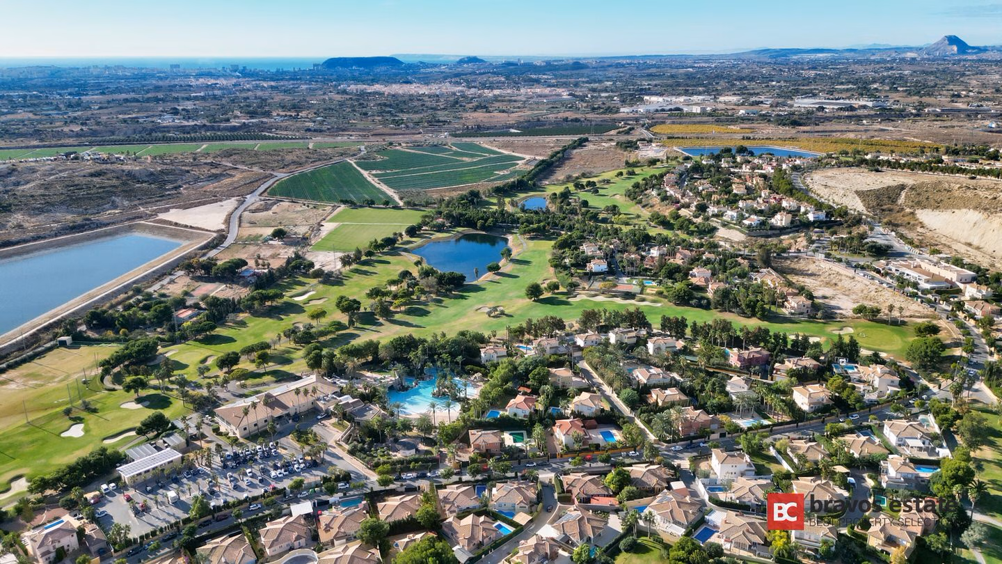 Vista aérea del complejo de golf de Bonalba Green en Mutxamel, con el campo de 18 hoyos, lagos, villas residenciales, piscinas comunitarias y montañas y mar al fondo.