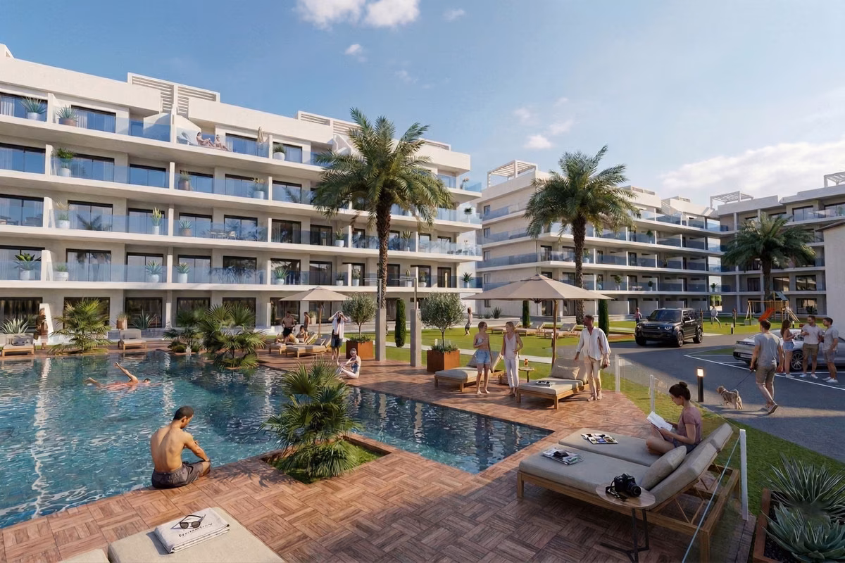 Communal pool with a timber-look deck, palms and loungers in front of the apartment blocks