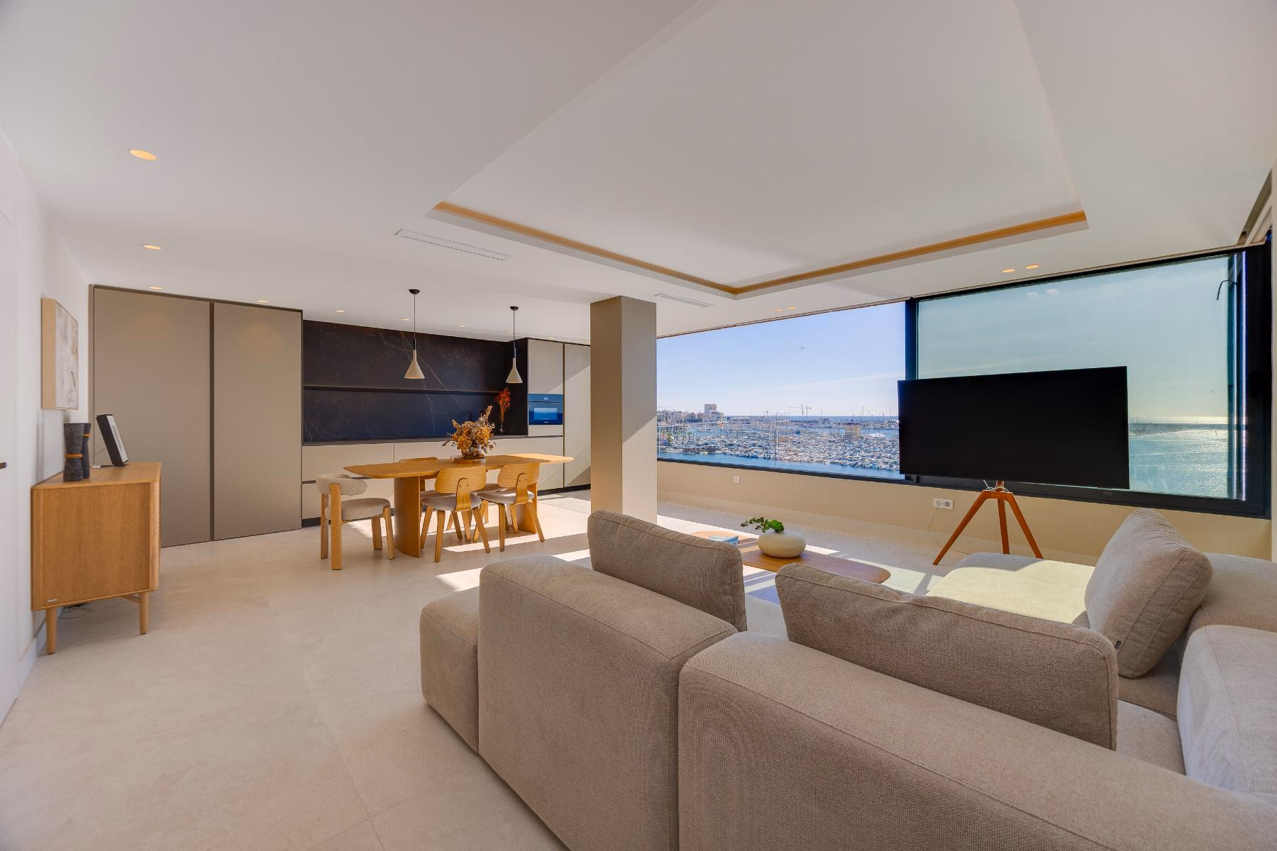 Living area with a beige sofa, TV on a stand and the window facing the sea