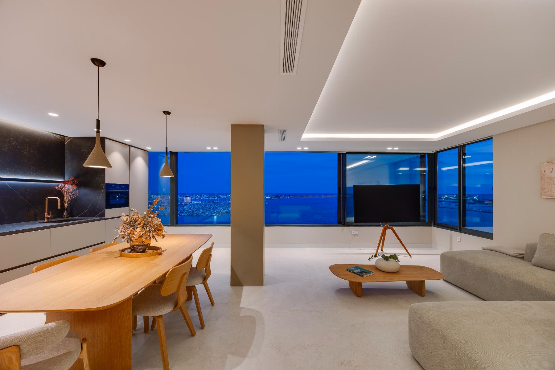 Dining table and open kitchen with dark stone splashback, sea view through the window