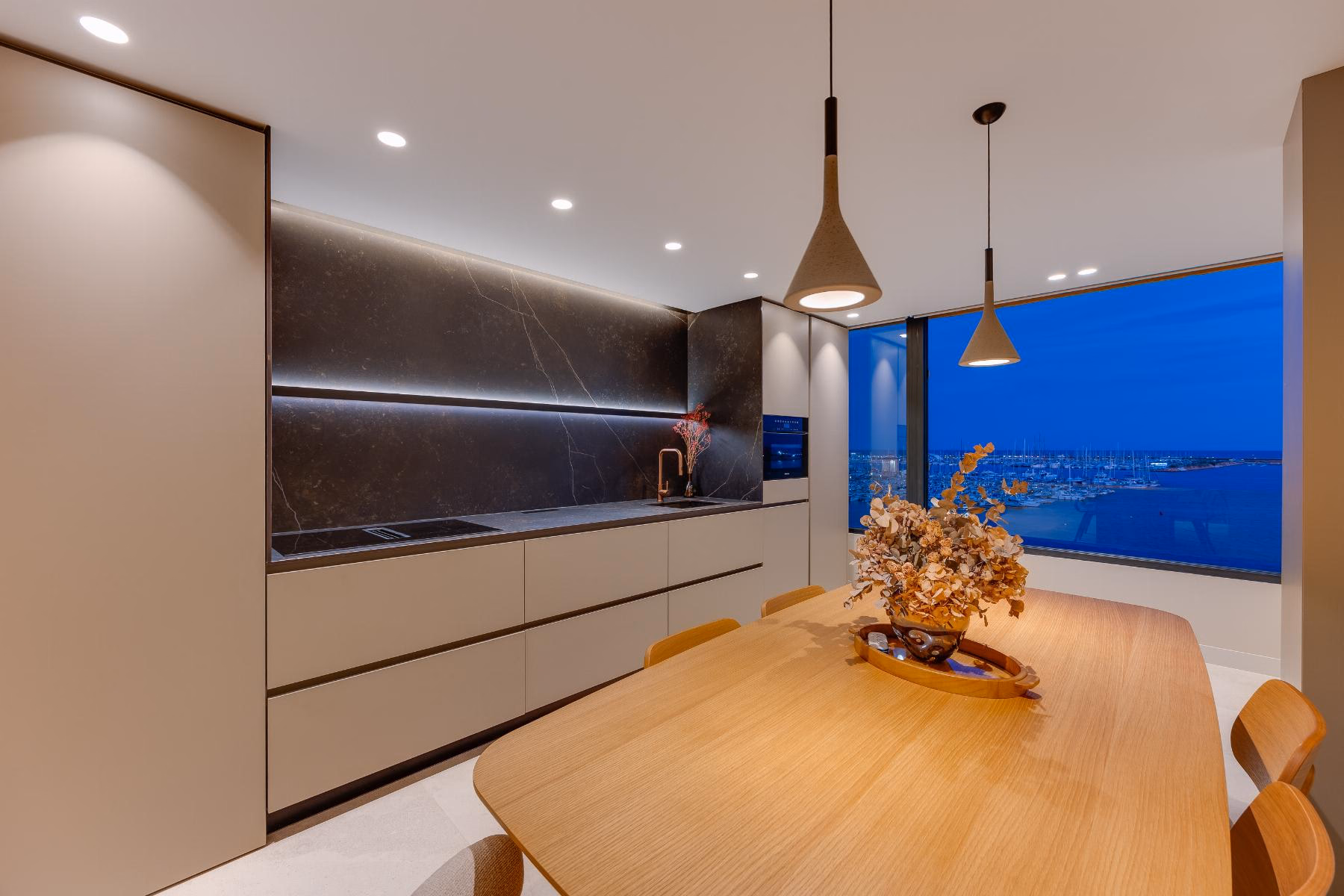 Kitchen with handleless units, dark splashback and pendant lamps over the table