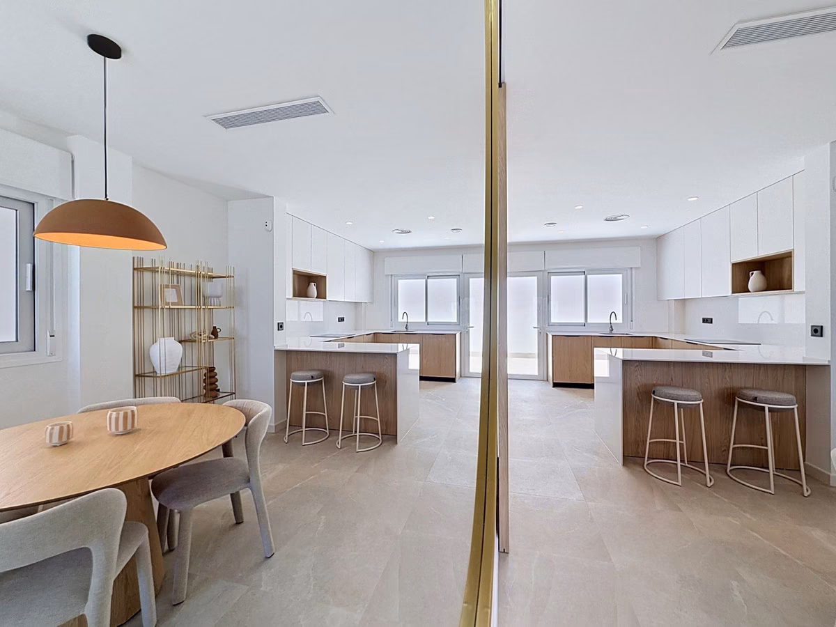 Open kitchen with a peninsula and bar stools reflected in a mirror, round dining table in front