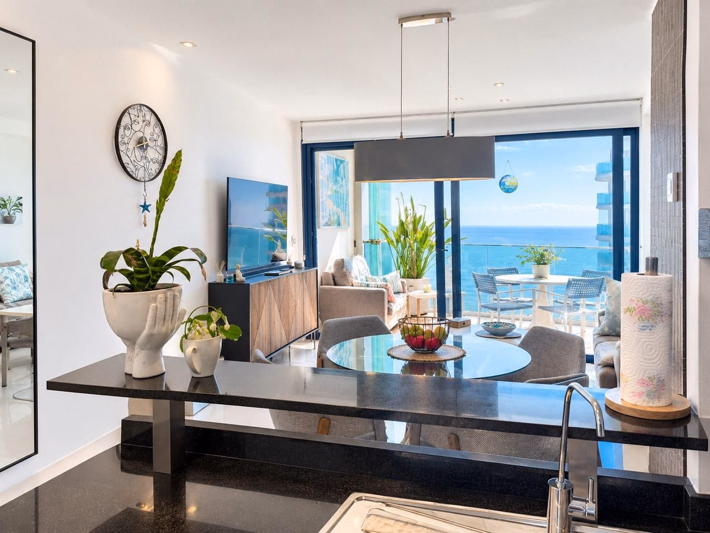 Mesa de comedor y lámpara colgante con la terraza acristalada y el mar detrás