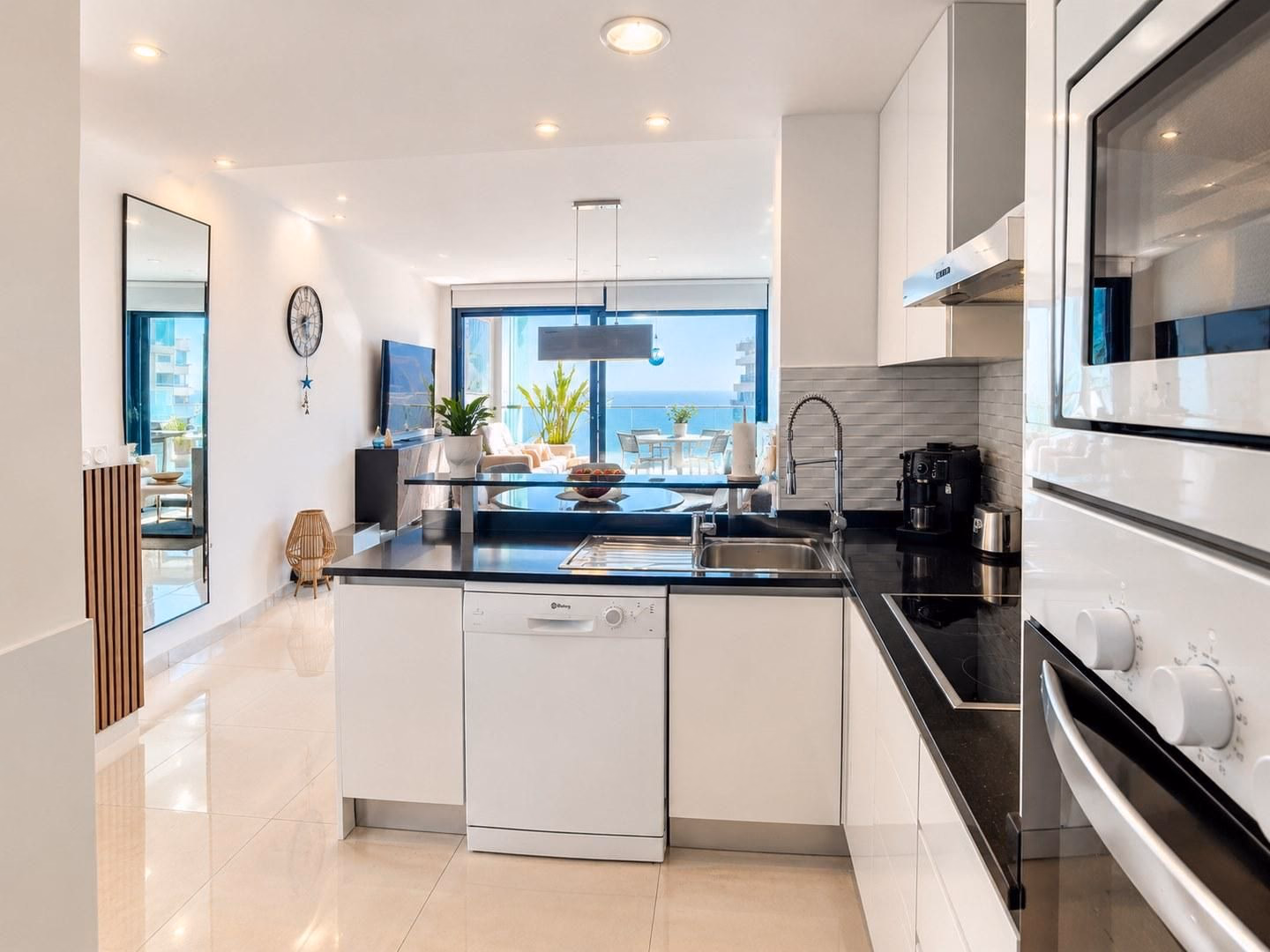 Cocina blanca con encimera negra, horno integrado y ventana hacia la terraza