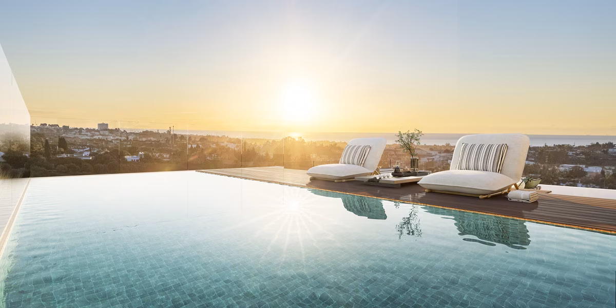 Bord de la piscine à débordement avec transats et la côte au coucher du soleil