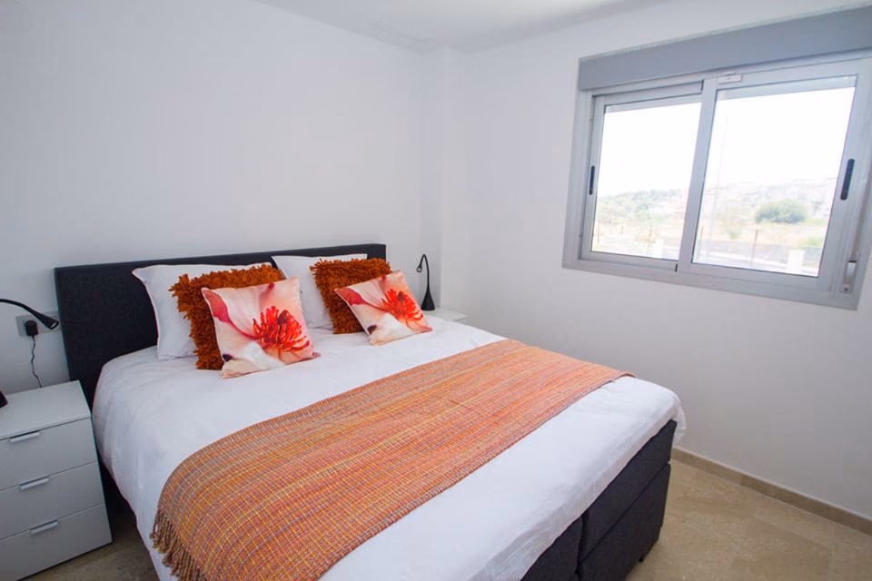 Bedroom with made-up double bed and orange cushions