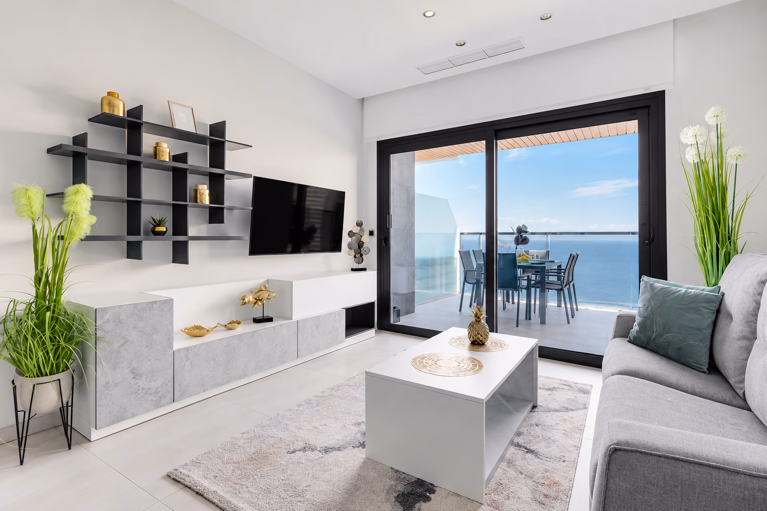 Wohnzimmer mit TV-Wand und Sofa, offen zur Terrasse und zum Meer