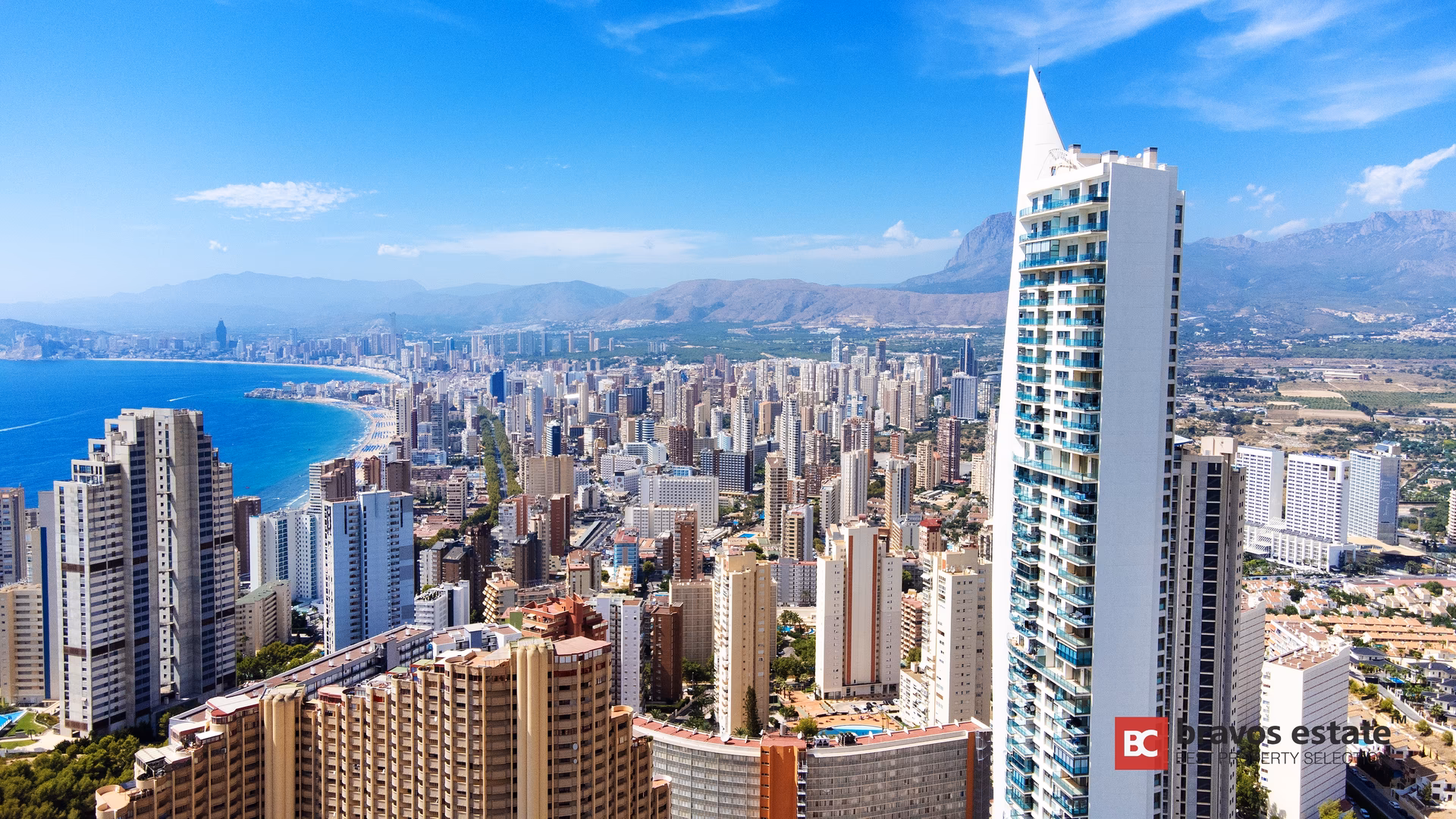 Torre Lugano, der weiße Turm mit spitzer Krone, über Benidorm mit dem Levante-Strand, der Skyline und den Bergen dahinter
