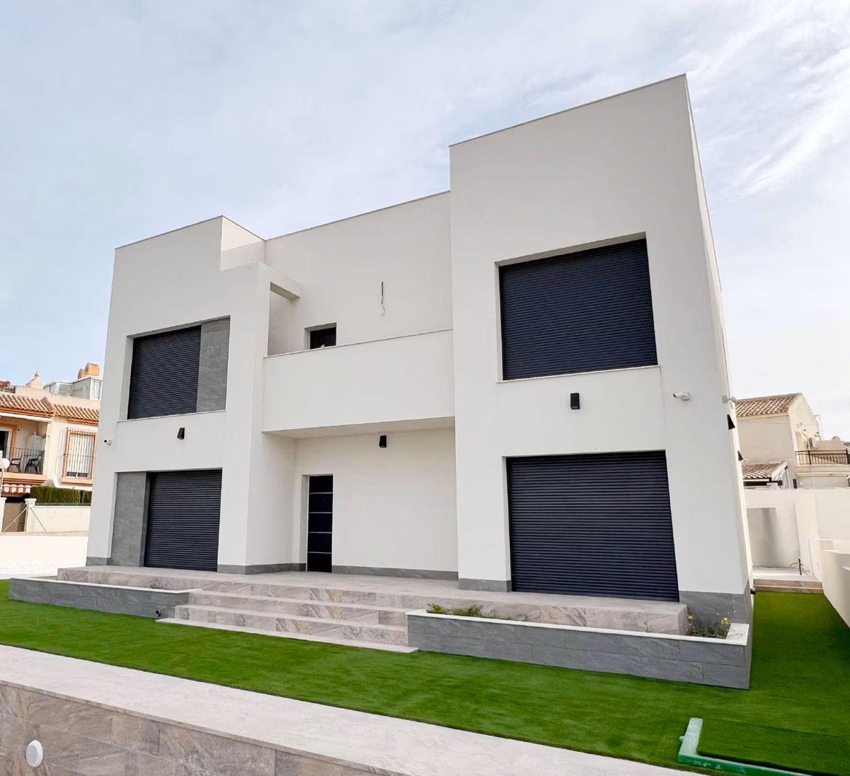 White two-storey villa with entrance steps and a lawn in front