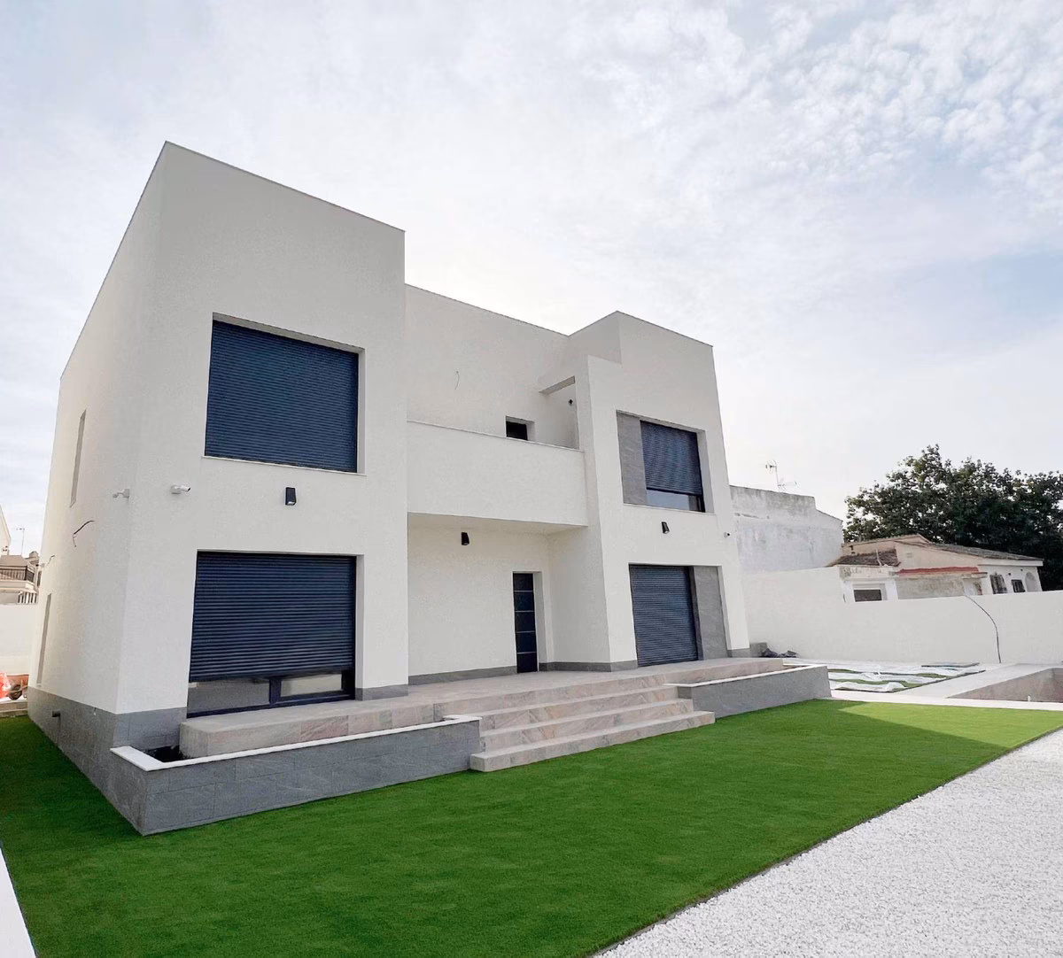 Villa with lawn, entrance steps and gravel path along the side