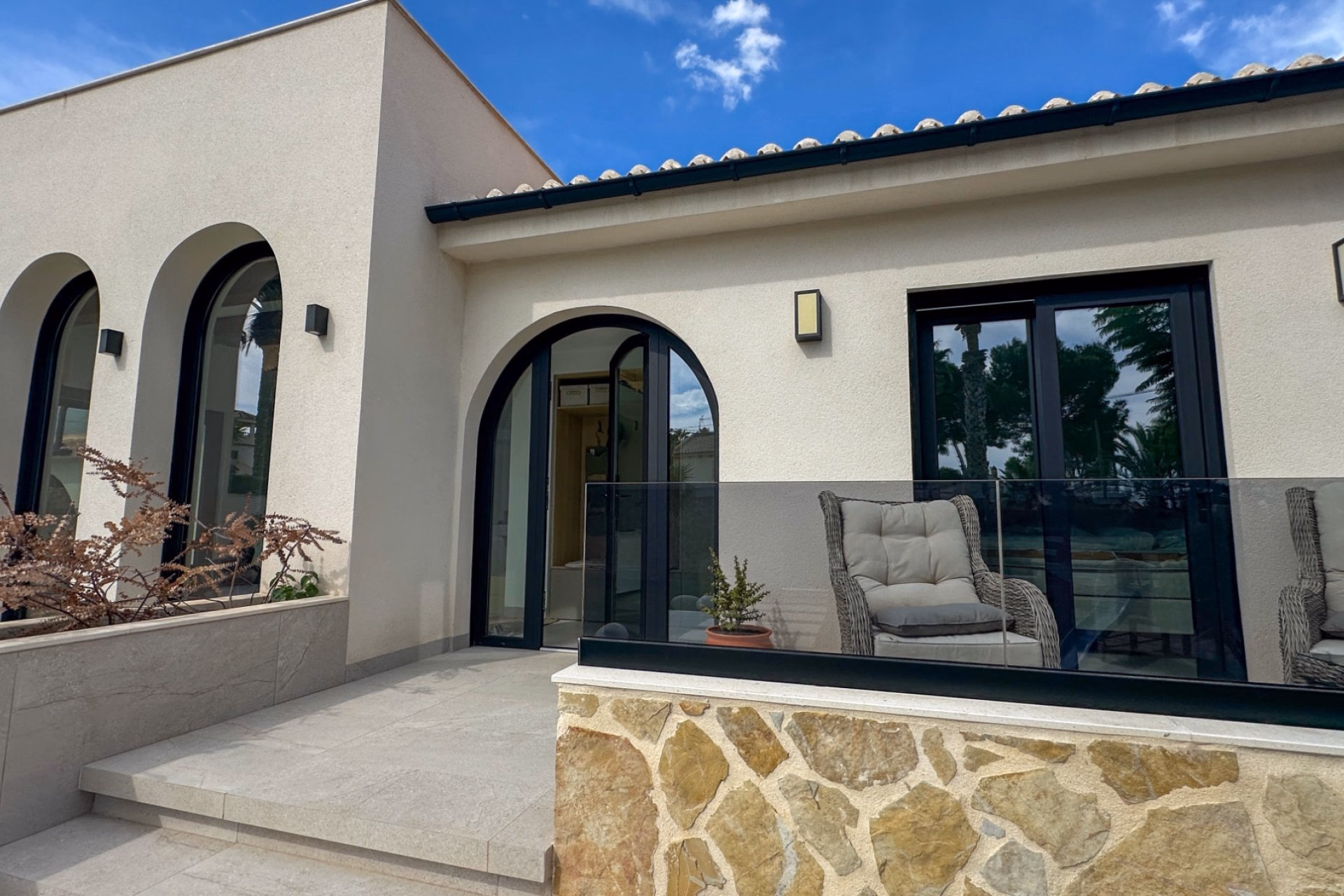 Side of the villa with arched glass doors and a paved terrace